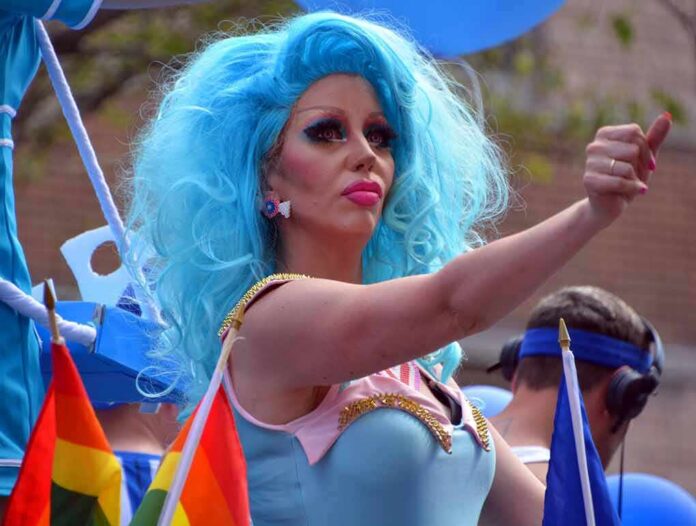Drag performer with bright blue wig giving thumbs up at parade