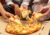 Hands pulling cheesy pizza slices from a box