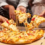 Hands pulling cheesy pizza slices from a box