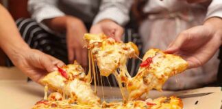 Hands pulling cheesy pizza slices from a box