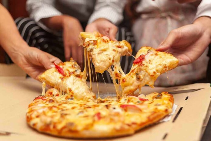 shutterstock_1163262373 Hands pulling cheesy pizza slices from a box