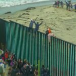 People climbing a tall beachside border fence