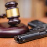Gavel beside a handgun on a wooden table