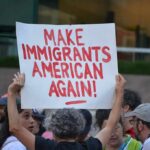 DNC Civil War: Abolish ICE Now, or Reform It Teddy Williams at a protest holding a sign reading 'Make Immigrants American Again'