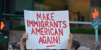 Teddy Williams at a protest holding a sign reading 'Make Immigrants American Again'