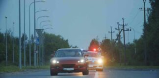 red car driving on road with police car behind using flashing lights
