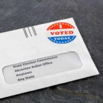 Maniac Socialist PULLS OFF Remarkable Win in Red State Absentee ballot envelope with I Voted sticker on dark surface
