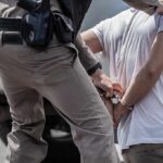 GOP Rep’s Son ARRESTED During Sting Operation police officer handcuffing a person beside a vehicle