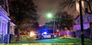 Police car blocks residential street at night behind caution tape
