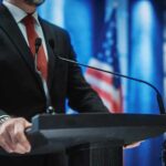 man in suit at podium with microphones