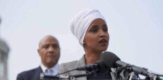 Ilhan Omar speaking at a podium with André Carson standing behind