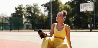 Woman in yellow activewear sitting on outdoor court with water bottle