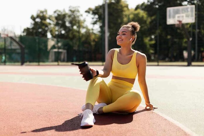 Woman in yellow activewear sitting on outdoor court with water bottle