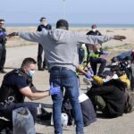 Police officers process group of people on a beachside pavement