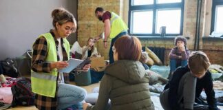 Volunteers assist people resting on mats in a temporary shelter