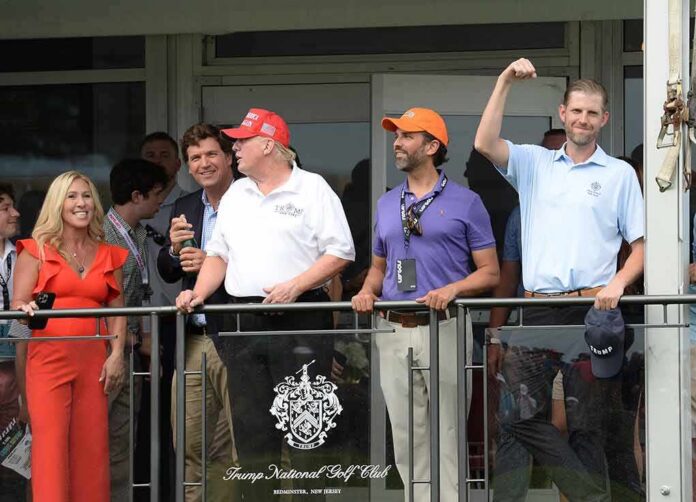 Eric Trump, Tucker Carlson, and Donald Trump Jr. on a balcony at a golf club event