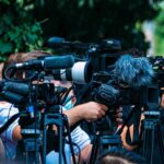 College Football Player Dies After Scoring Touchdown TV news cameras crowding together at an outdoor event