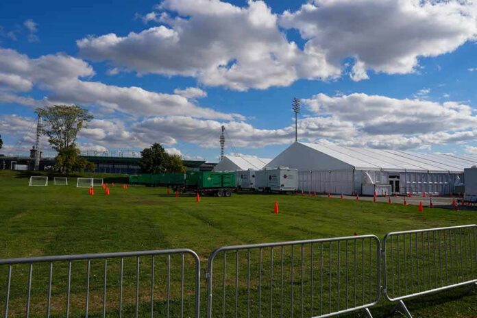 shutterstock_2216173395 Temporary white tents and equipment on a grassy field with traffic cones and metal barriers