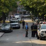 City Erupts After Brutal Migrant Stabbing Police officers secure a residential street with patrol cars and yellow tape