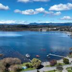 Google INFURIATES Canada With Latest Update Aerial view of a lakeside town with pier and boats under a blue sky