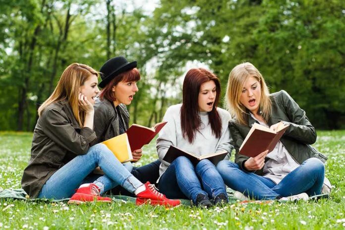 Group of young women reading books on grass in a park