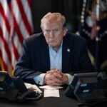 Trump Takes WRECKING BALL To JFK Memorial Person in suit seated at table with telephones