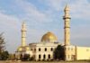 Mosque with golden dome and two tall minarets under a partly cloudy sky