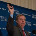 Man in suit speaking at podium holding up a smartphone