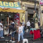 Street taco stand with people and a religious statue on a sidewalk