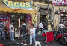 Street taco stand with people and a religious statue on a sidewalk