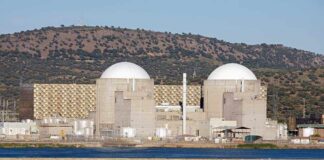 Nuclear power plant with domed structures beside a water body and mountains in the background