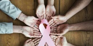 Hands forming a circle around a pink ribbon on a wooden table