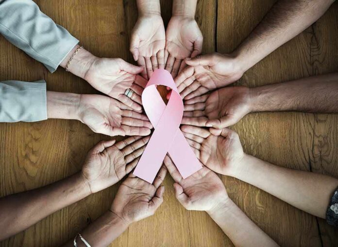 Hands forming a circle around a pink ribbon on a wooden table