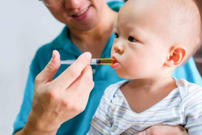 Baby taking liquid medicine from an oral syringe held by an adult