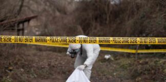 forensic investigator at outdoor crime scene behind caution tape