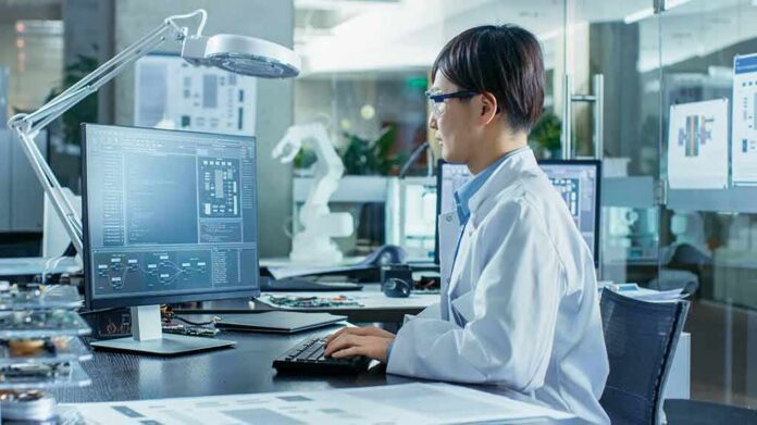 Engineer in lab coat working at a computer in a modern lab