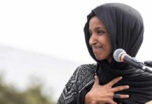 Ilhan Omar Breaks Silence After Feds Raid Her Home Ilhan Omar speaking at a microphone with hand on chest