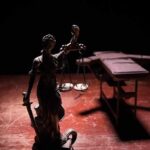 Lady Justice statue with scales in dramatic light beside an empty gurney
