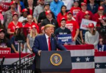 Donald Trump speaks at a rally podium; Christian Jones and Bear Pascoe are in the crowd behind him