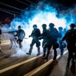 Riot police advance through tear gas at night on a city street