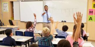 Teacher at front of classroom as students raise hands