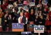 Donald Trump addresses a rally crowd at a podium, raising his fist