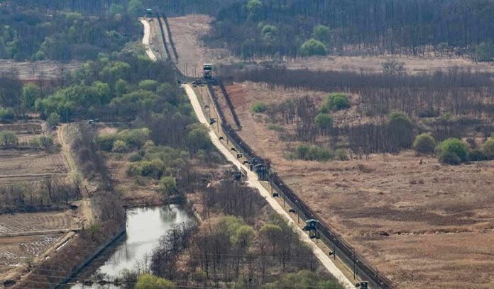 Border fence and patrol road cutting through dry landscape with sparse trees
