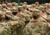 Soldiers in camouflage uniforms salute in formation