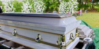 White casket surrounded by flowers at a burial site.
