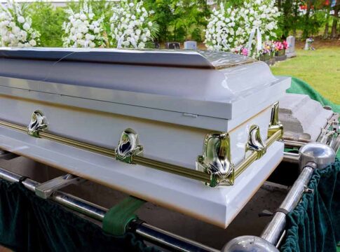White casket surrounded by flowers at a burial site.
