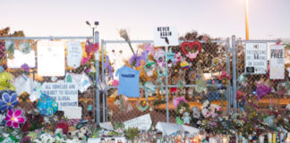 Memorial with candles, flowers, and signs against metal fence.
