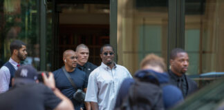 Group of men exiting building with photographers nearby