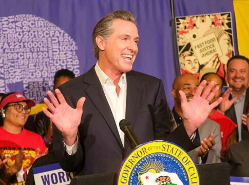 Man speaking at podium with smiling audience behind.