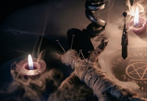 A dark, mystical scene featuring candles, a voodoo doll, and occult symbols